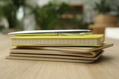 Stack of planners and pen on wooden table indoors, closeup