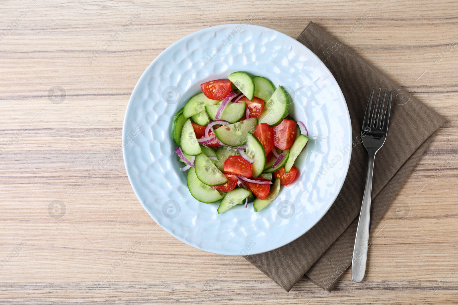 Photo of Plate of tasty cucumber tomato salad served on wooden table, flat lay