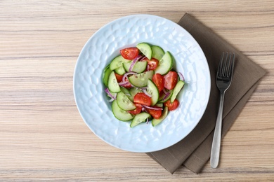 Photo of Plate of tasty cucumber tomato salad served on wooden table, flat lay