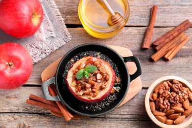 Tasty baked apple with nuts in baking dish, honey and cinnamon sticks on wooden table, flat lay