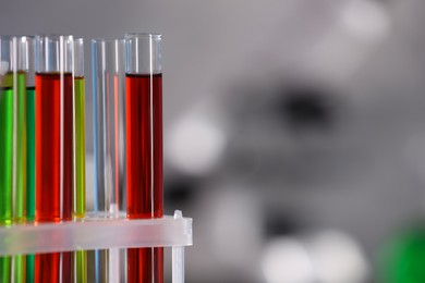Laboratory test tubes with colorful liquids against blurred background, closeup. Space for text