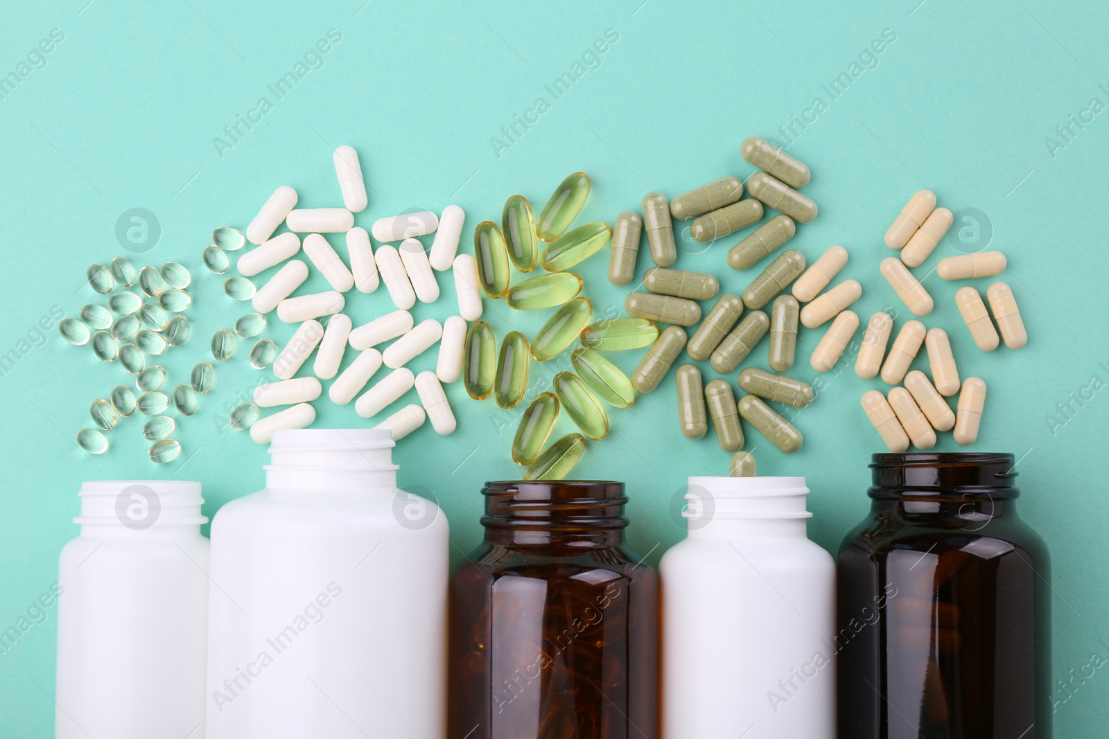 Photo of Bottles and different vitamin capsules on turquoise background, flat lay