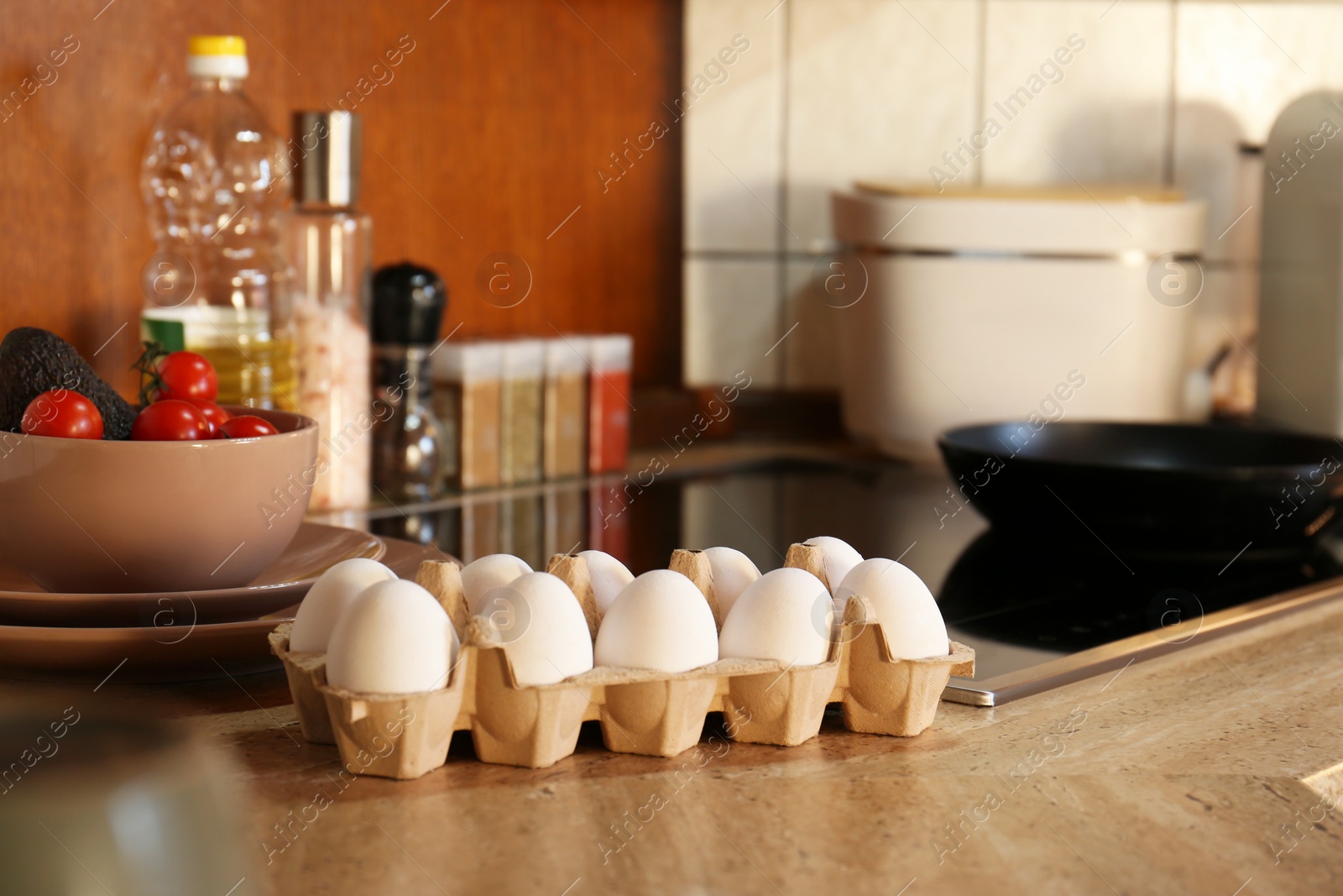 Photo of Many fresh eggs in carton, cucumber and tomatoes on wooden table in kitchen. Ingredients for breakfast