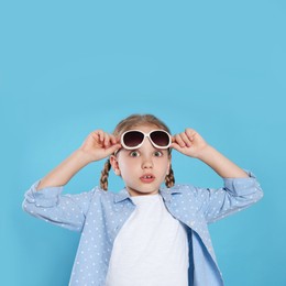 Photo of Emotional girl wearing stylish sunglasses on light blue background