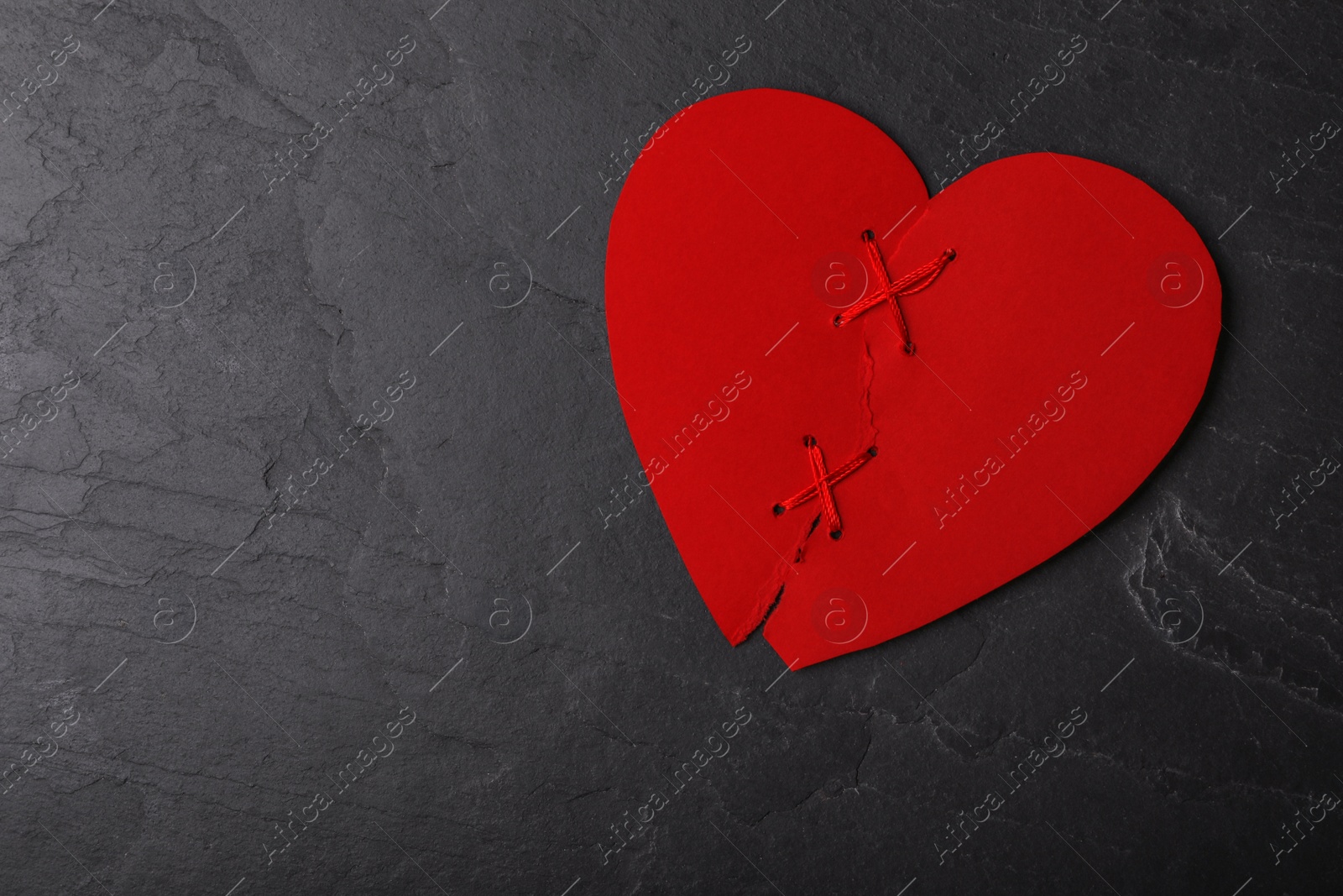 Photo of Top view of torn paper heart sewed with thread on black stone background, space for text. Relationship problems concept