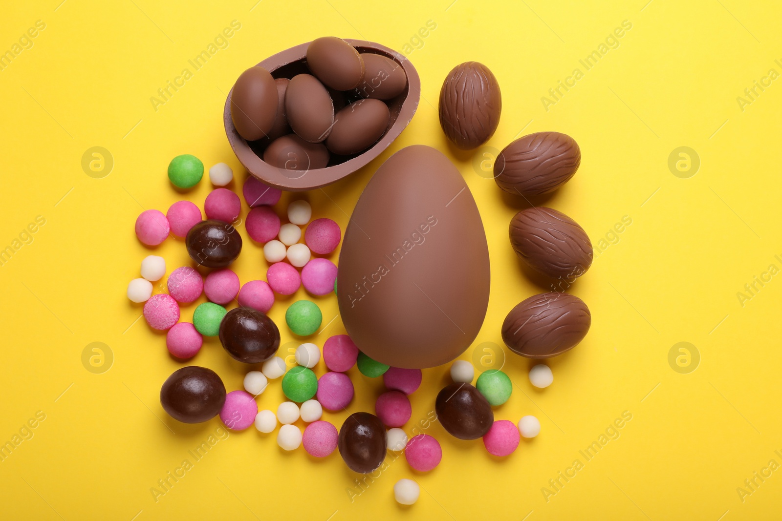 Photo of Delicious chocolate eggs and candies on yellow background, flat lay