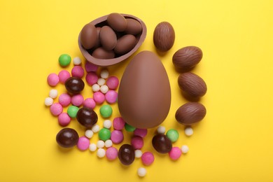Photo of Delicious chocolate eggs and candies on yellow background, flat lay