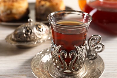 Photo of Glass of traditional Turkish tea in vintage holder on white wooden table, closeup