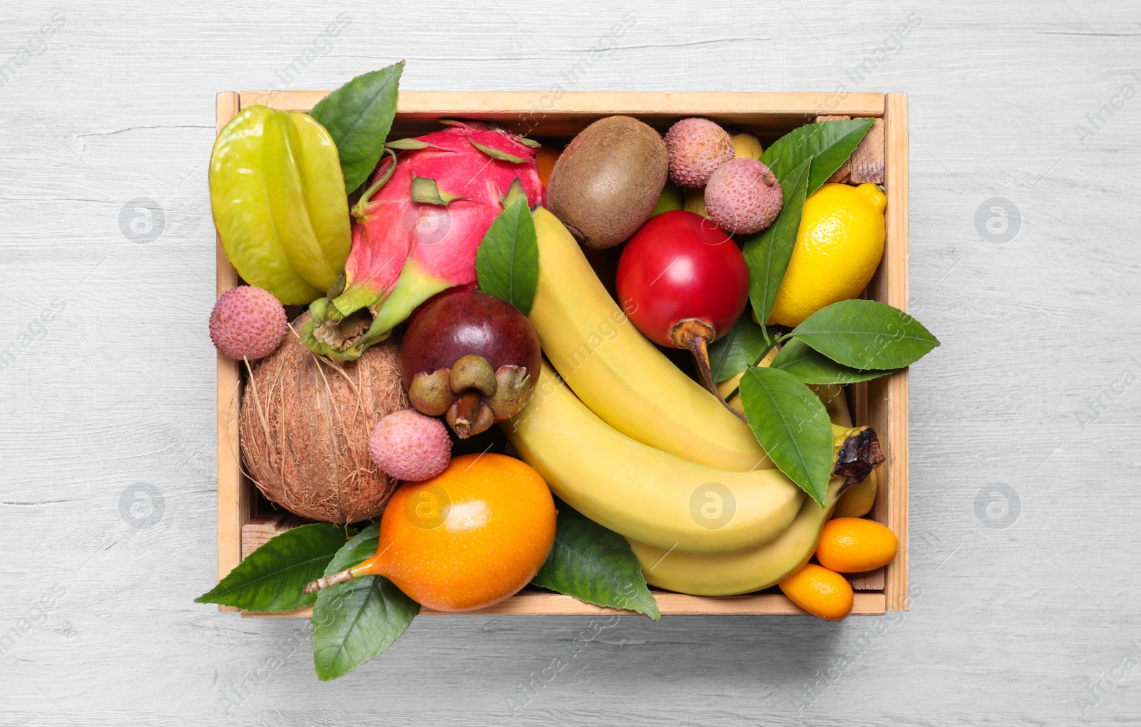 Photo of Crate with different exotic fruits on white wooden table, top view