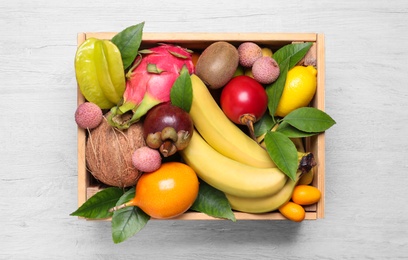 Crate with different exotic fruits on white wooden table, top view