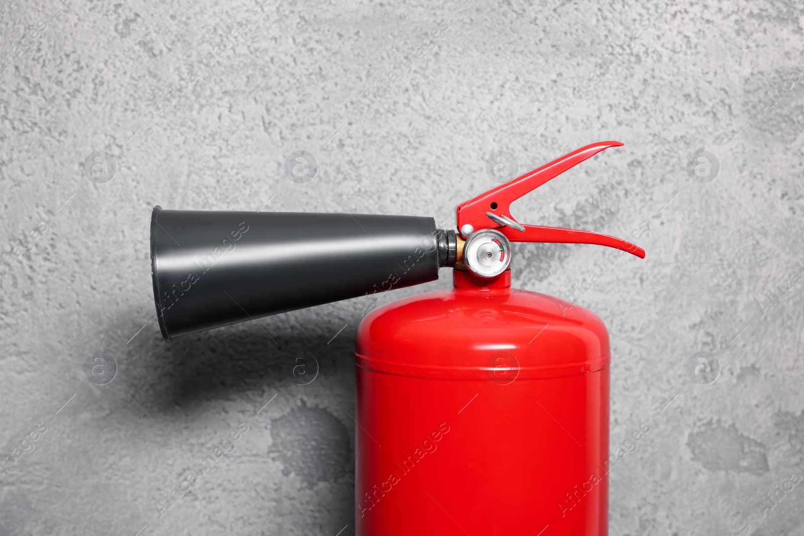Photo of Red fire extinguisher near grey wall, closeup