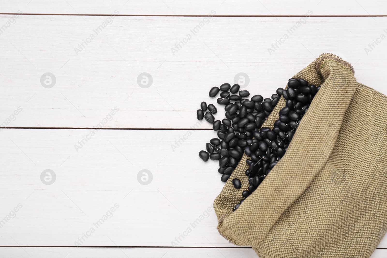 Photo of Sack of raw black beans on white wooden table, top view. Space for text