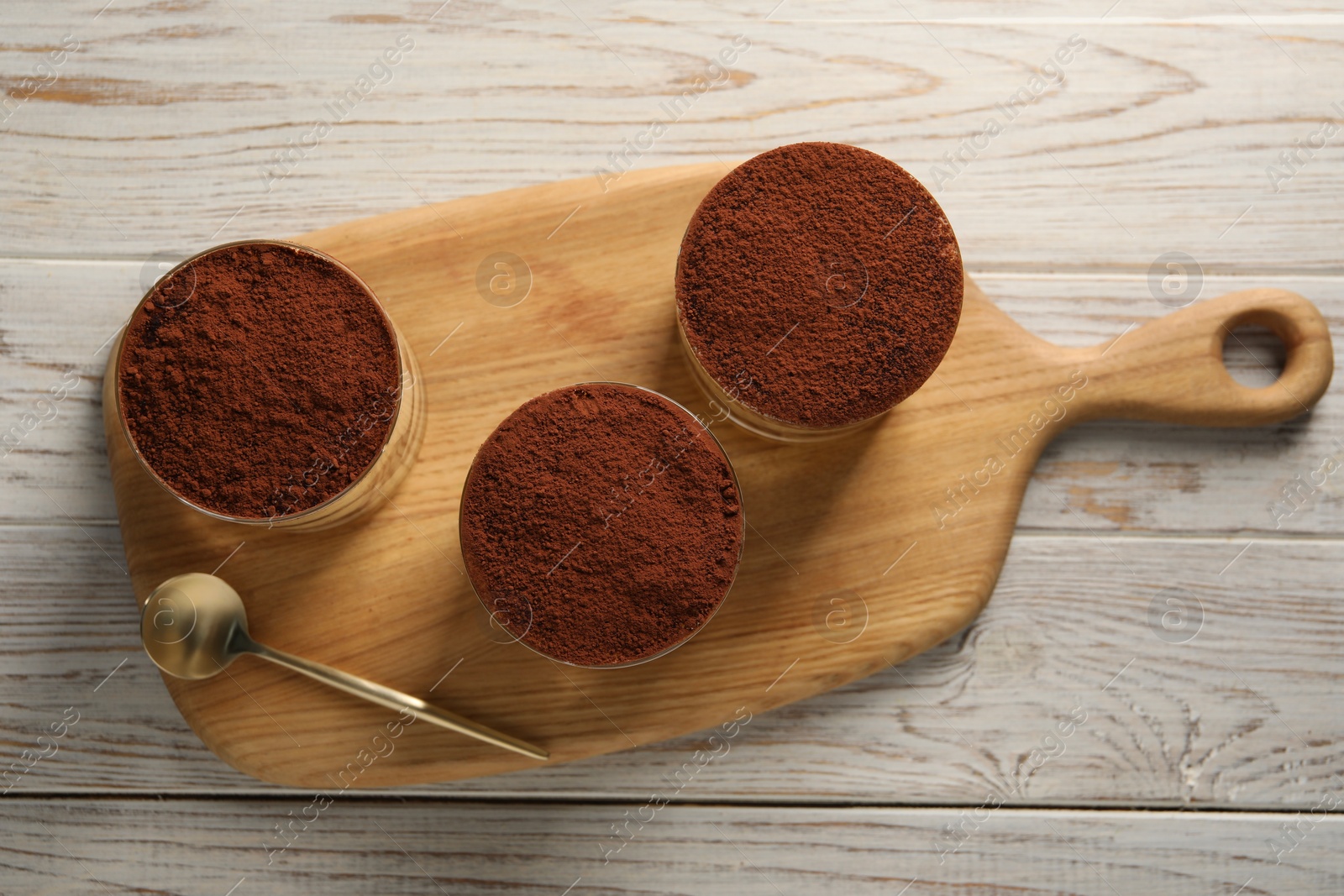 Photo of Delicious tiramisu in glasses and spoon on light wooden table, top view