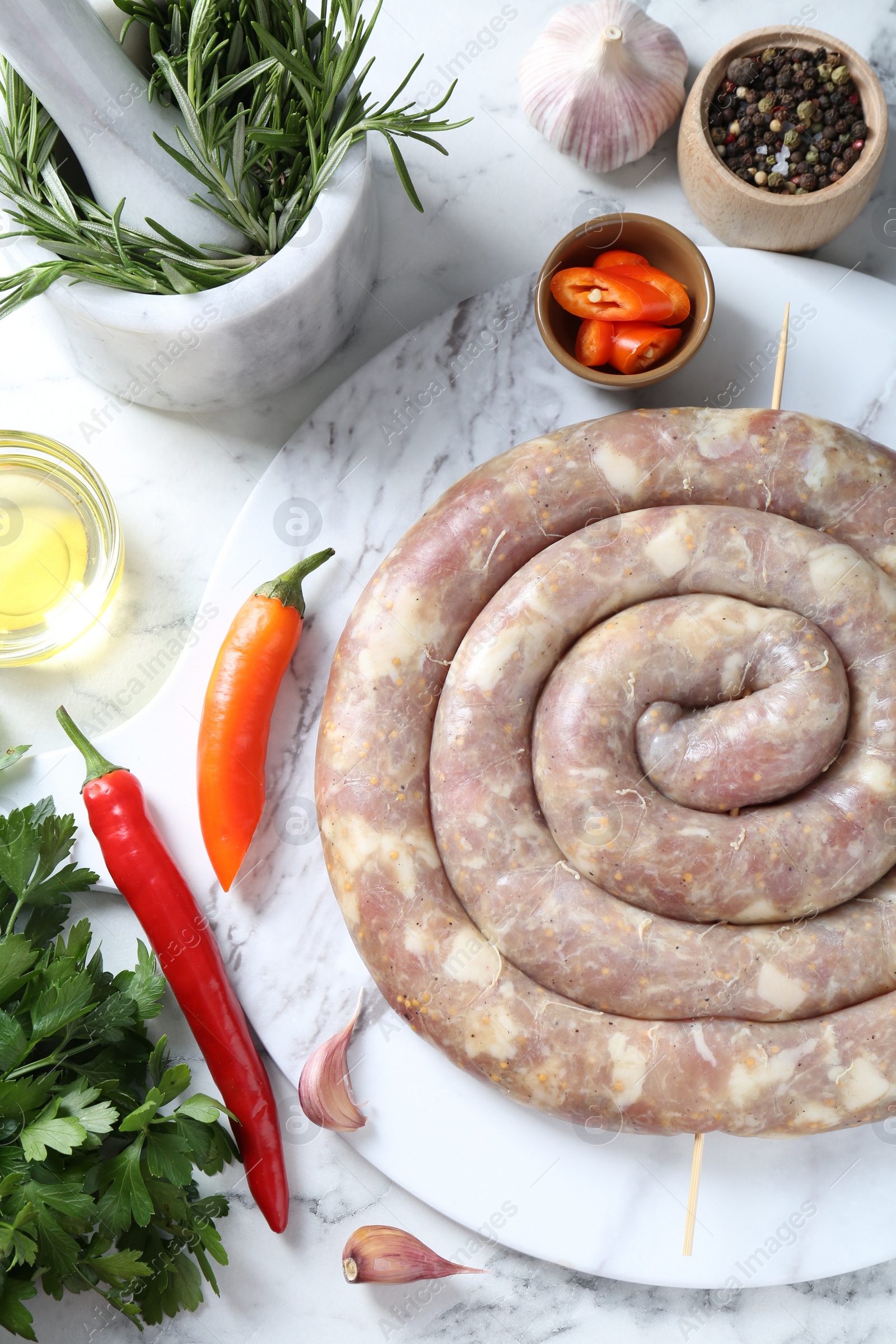 Photo of Raw homemade sausage, spices and other products on white marble table, flat lay