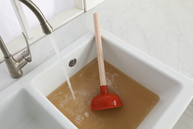 Photo of Clogged kitchen sink with plunger and dirty water
