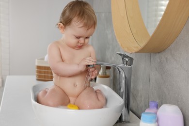 Cute little baby bathing in sink indoors