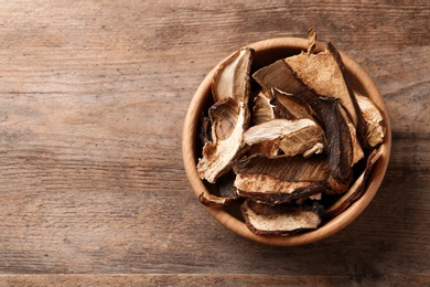 Bowl of dried mushrooms on wooden background, top view with space for text