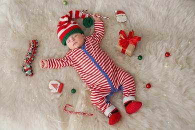 Photo of Cute little baby with Christmas candy cane sleeping on fluffy blanket, top view