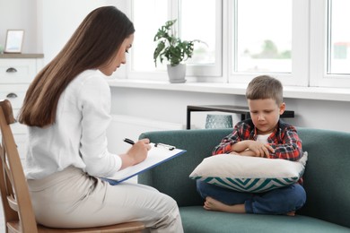 Photo of Psychologist working with unhappy little boy in office. Mental health problems