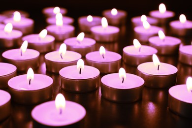 Beautiful burning violet candles on black background. Funeral attributes