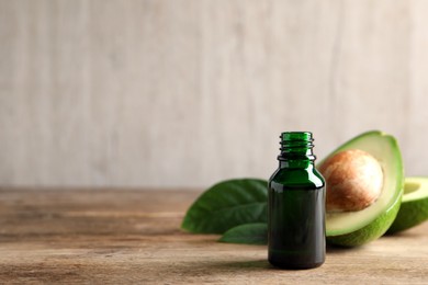 Photo of Bottle of essential oil, green leaves and fresh avocado on wooden table, space for text