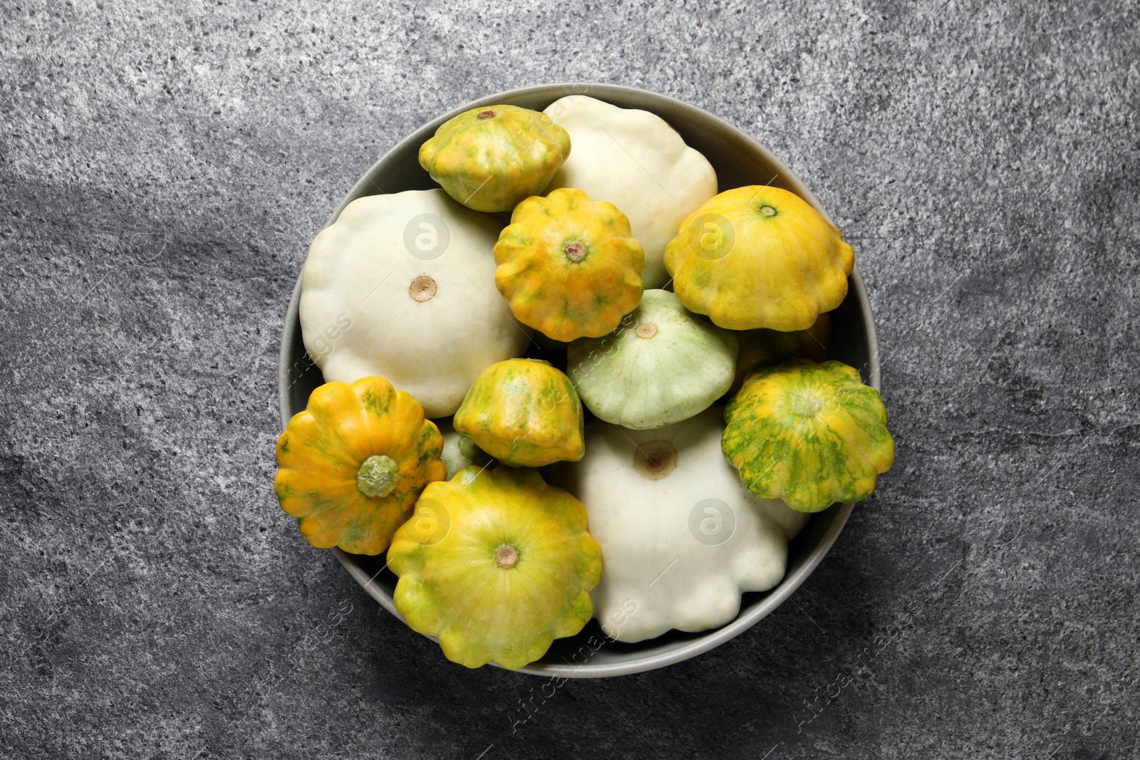 Photo of Fresh ripe pattypan squashes in bowl on grey table, top view