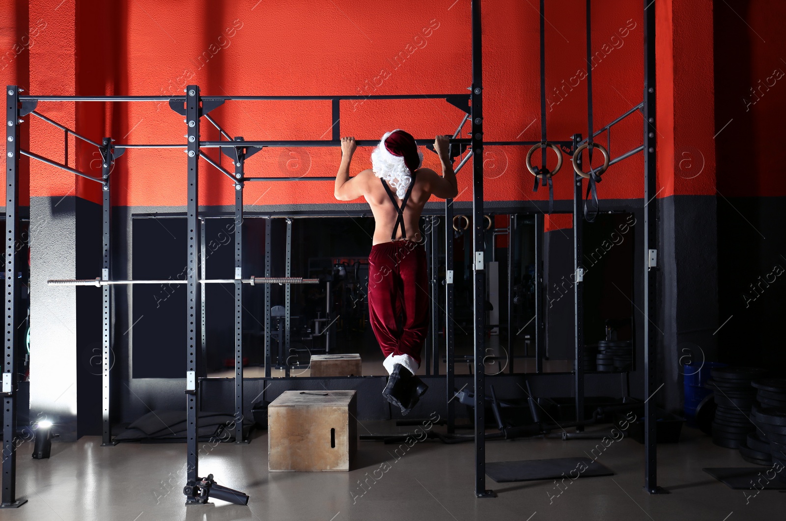 Photo of Young shirtless Santa Claus training in modern gym, back view