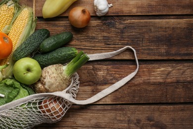 Photo of Different fresh vegetables in net bag on wooden table, flat lay. Farmer harvesting