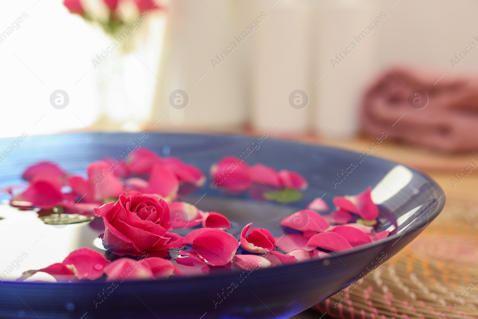 Photo of Pink roses and petals in bowl with water on table, closeup