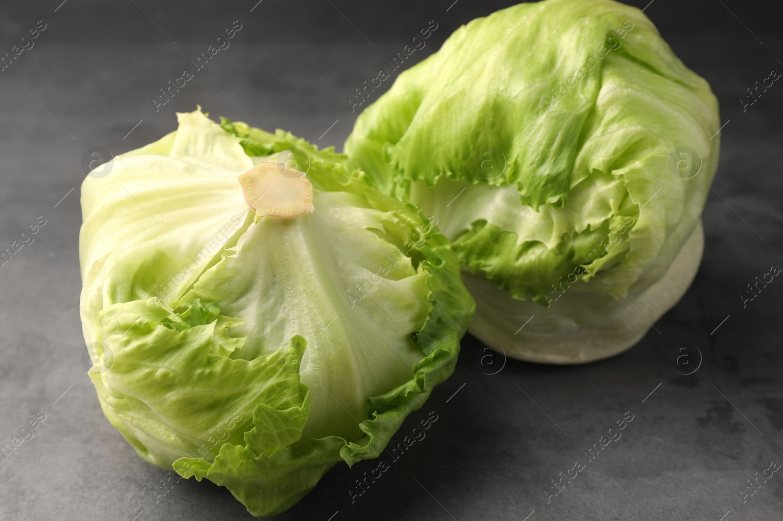 Photo of Fresh green iceberg lettuce heads on grey textured table, closeup