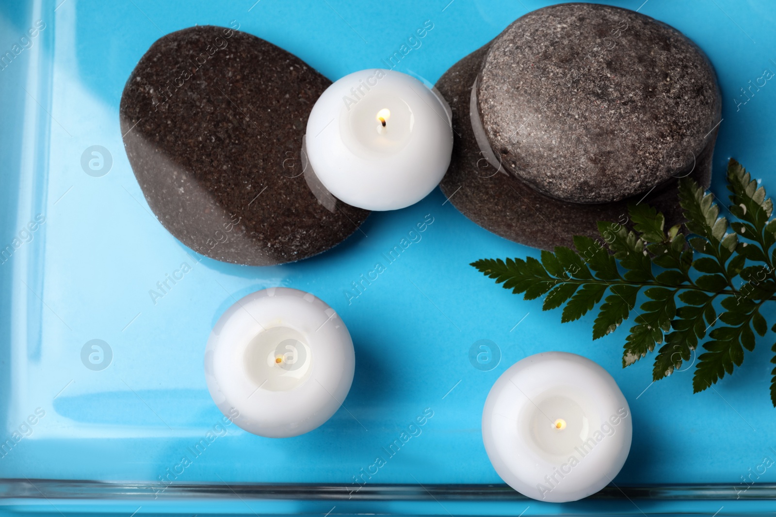 Photo of Burning candles, green leaf and spa stones in water, top view