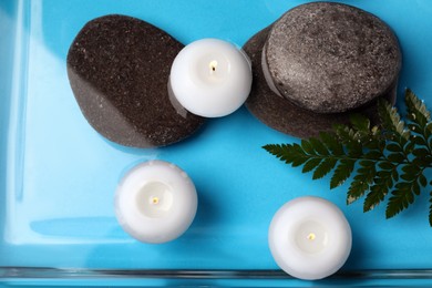 Burning candles, green leaf and spa stones in water, top view