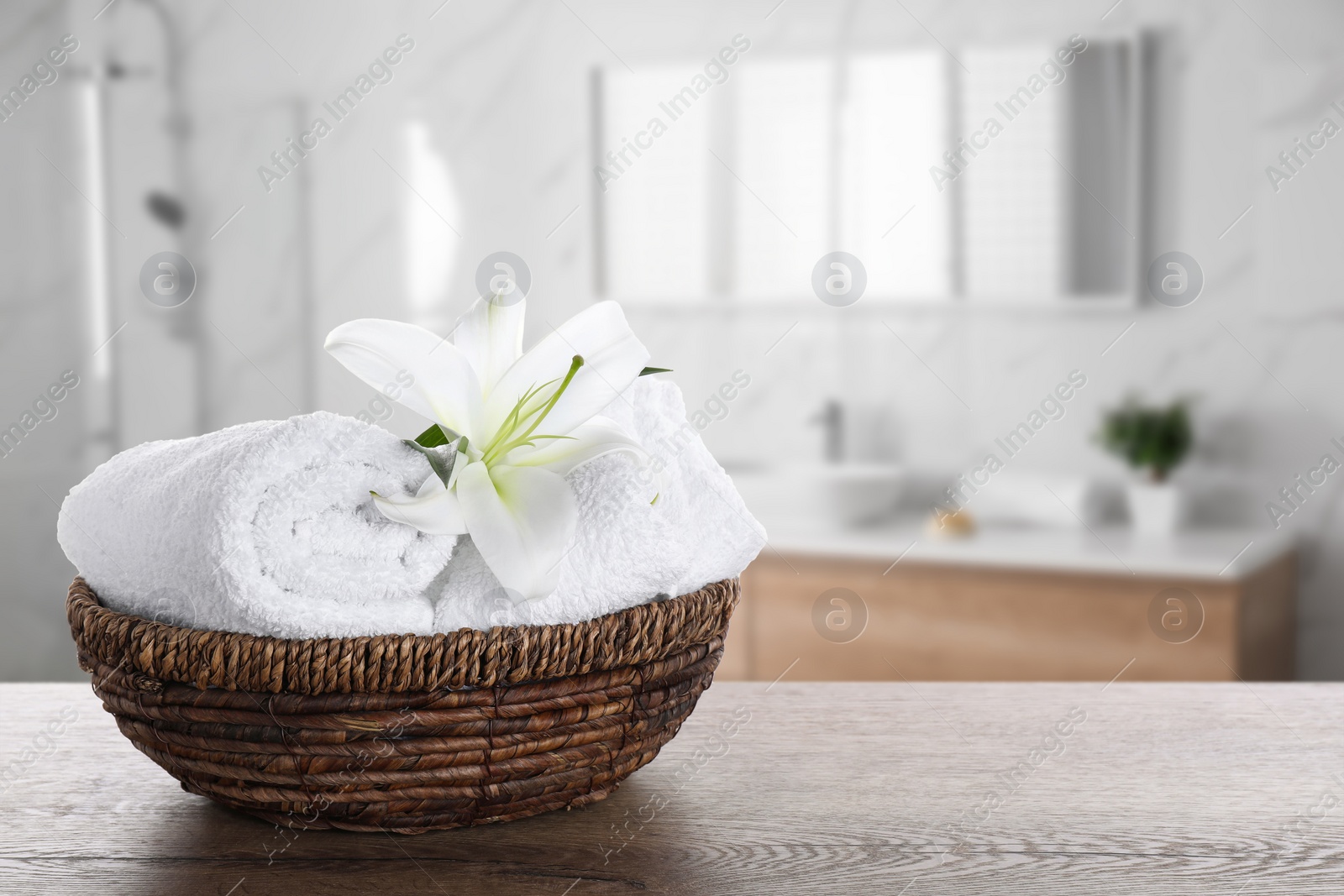 Image of Fresh towels and lily flower on wooden table in bathroom. Space for text
