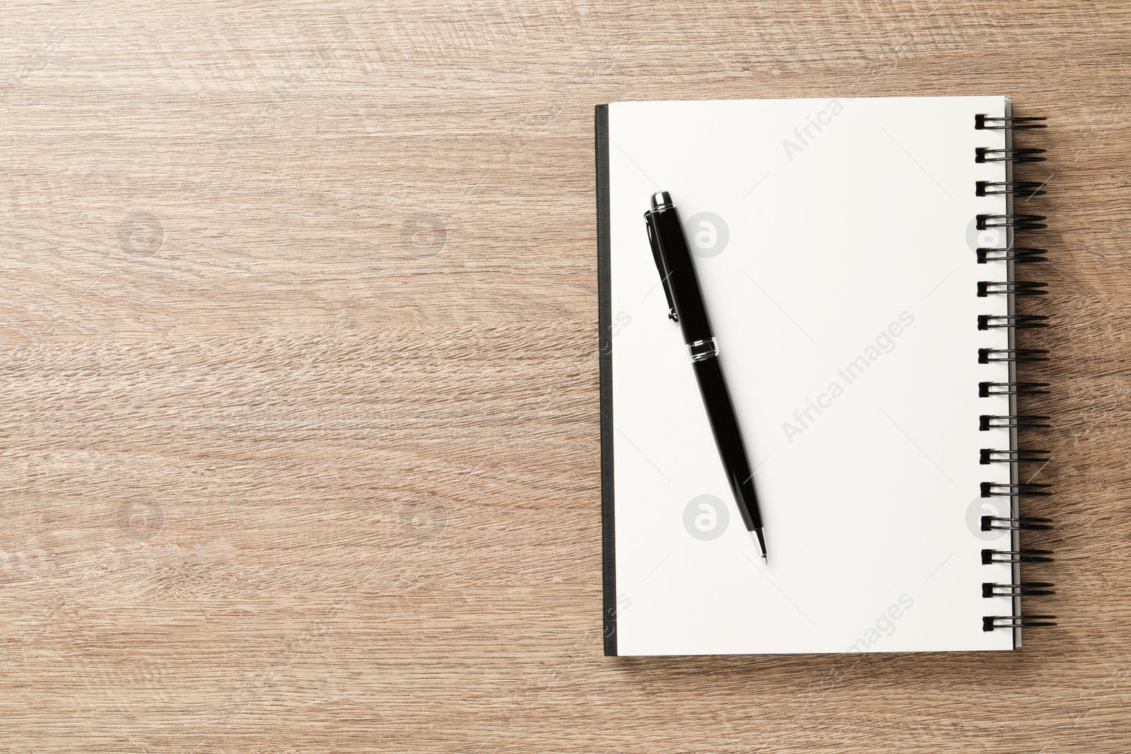 Photo of Notebook and pen on wooden table, top view. Space for text