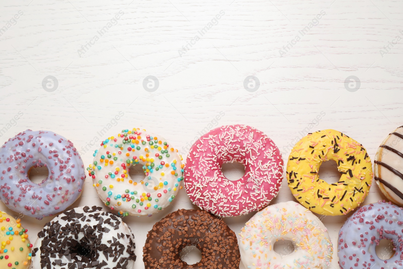 Photo of Delicious glazed donuts on white wooden table, flat lay. Space for text