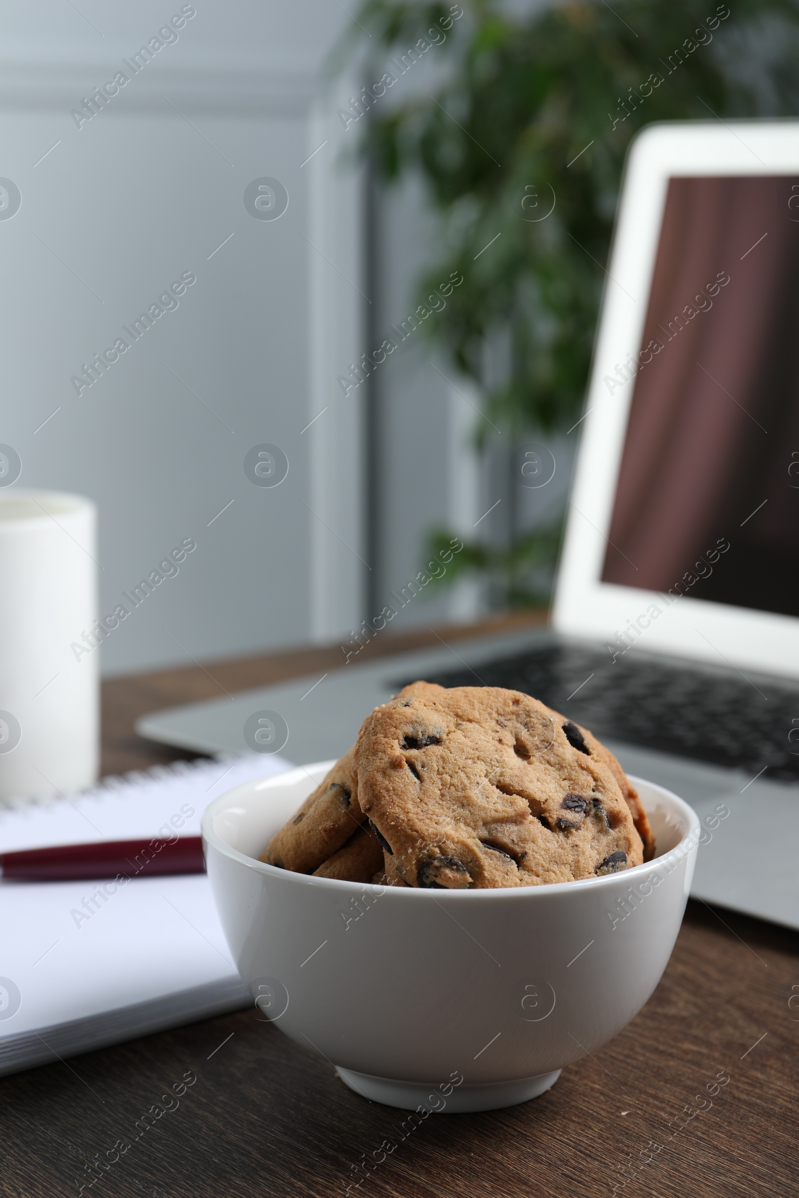 Photo of Bowl with chocolate chip cookies on wooden table in office