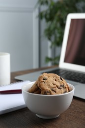 Bowl with chocolate chip cookies on wooden table in office