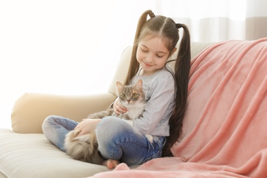 Photo of Cute little girl with cat sitting on sofa at home