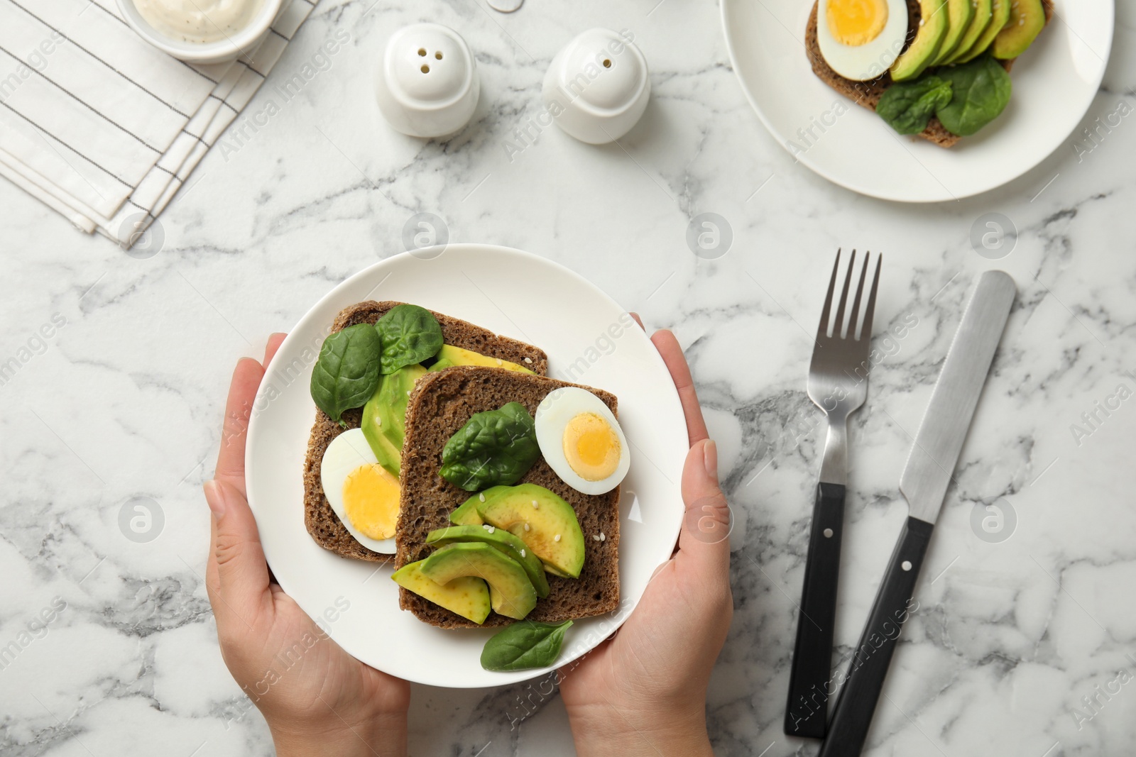 Photo of Woman with tasty avocado toasts at white marble table, top view