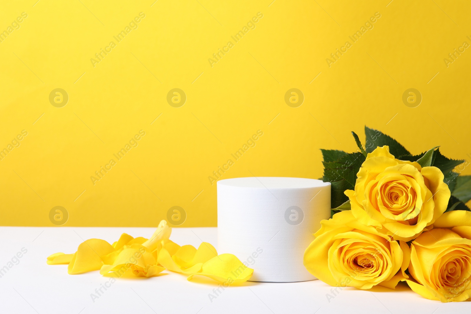 Photo of Beautiful presentation for product. Round podium and roses on white table against yellow background, space for text