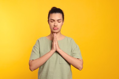 African American woman with clasped hands praying to God on orange background