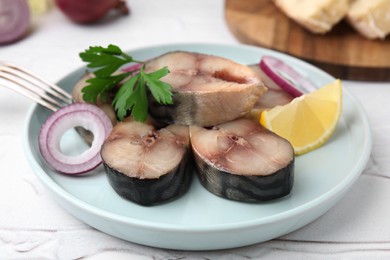 Slices of tasty salted mackerel with parsley, onion ring and lemon wedge on light table, closeup