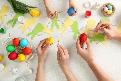 Photo of Father, mother and their child painting Easter eggs at wooden table, top view