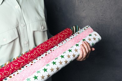 Photo of Woman holding different colorful wrapping paper rolls on grey background, closeup