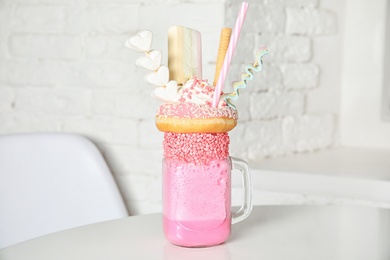 Photo of Tasty milk shake with sweets in mason jar on table at cafe