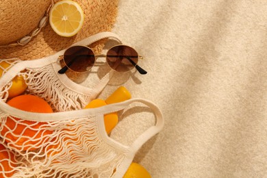 Photo of String bag with sunglasses, straw hat and fruits on beige textured background, flat lay. Space for text