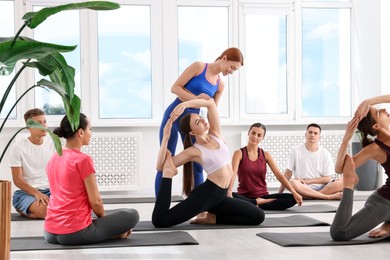 Photo of Yoga coach helping woman during group lesson indoors