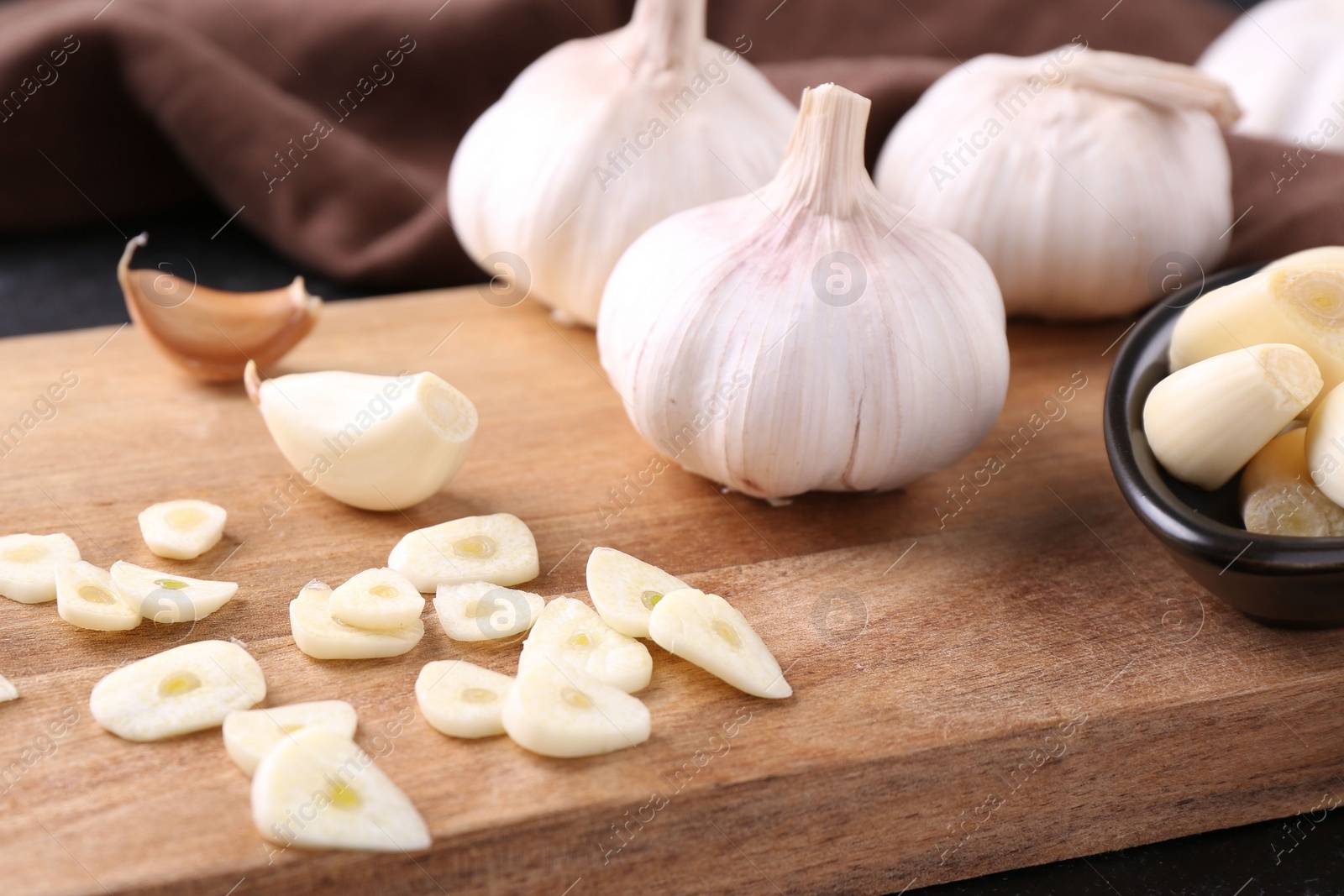 Photo of Aromatic cut garlic, cloves and bulbs on wooden board, closeup