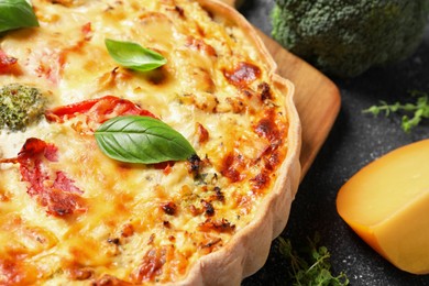 Tasty quiche with tomatoes, basil and cheese on dark textured table, closeup