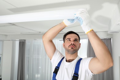 Photo of Electrician installing led linear lamp indoors. Ceiling light